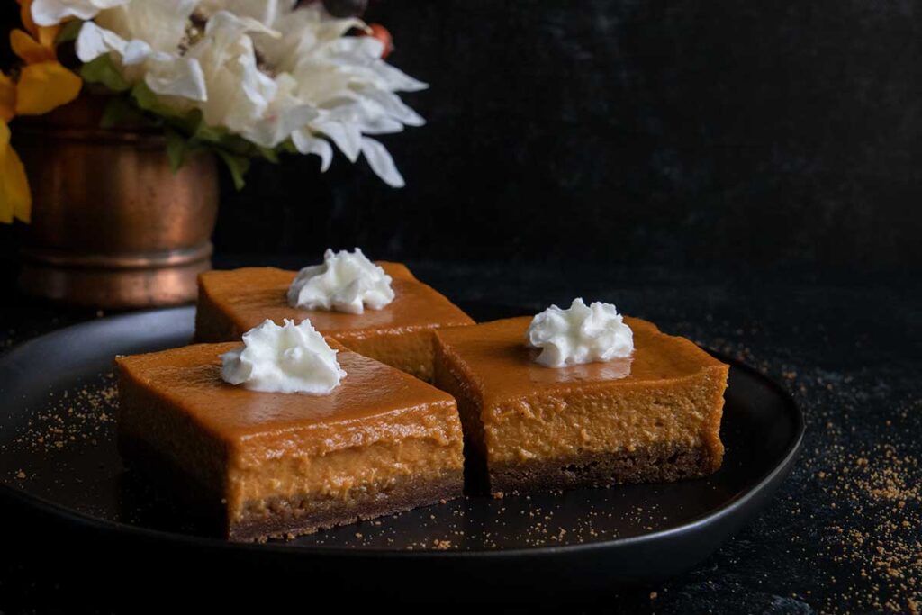 Pumpkin pie bars on a black plate garnished with whipped cream.