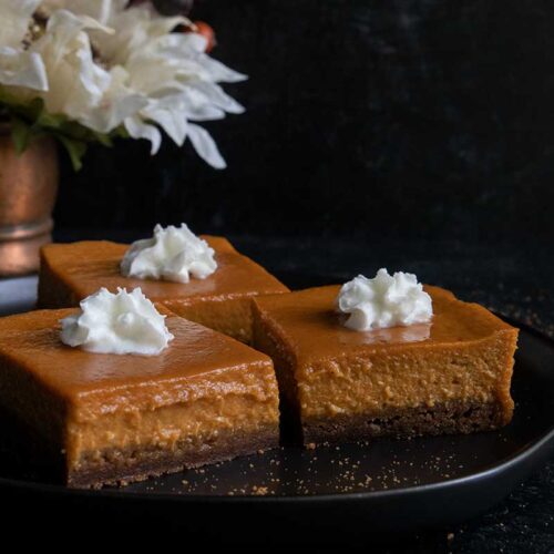 Pumpkin pie bars on a black plate garnished with whipped cream.