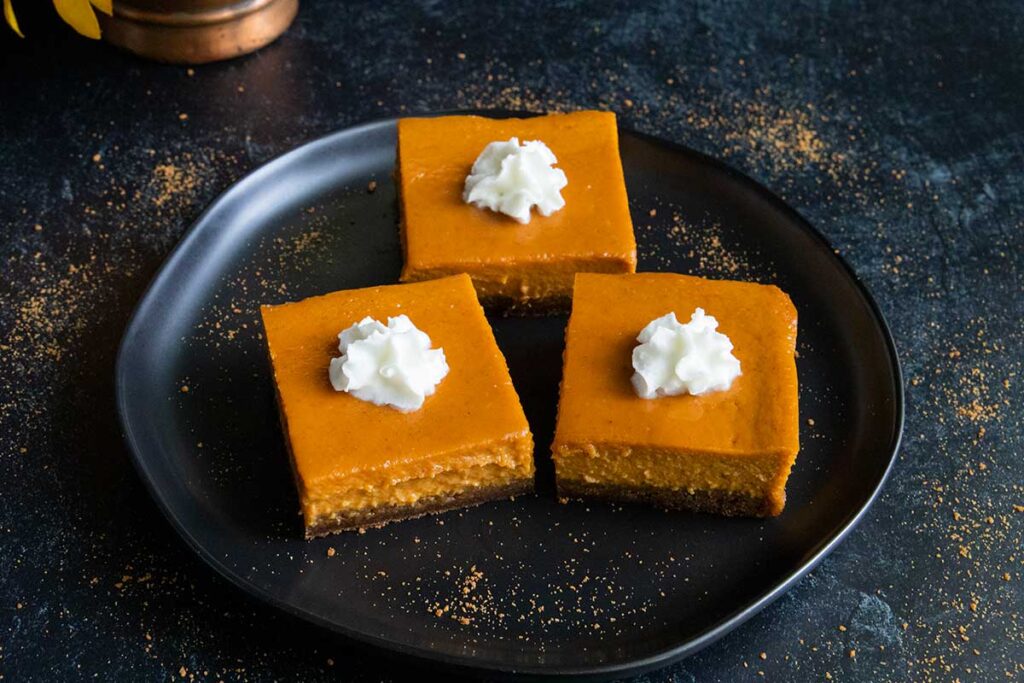 Pumpkin pie bars on black plate garnished with whipped cream.