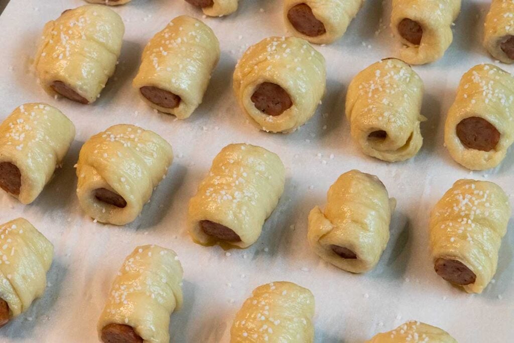 unbaked sausage pretzel bites with egg wash and pretzel salt on a cooking sheet