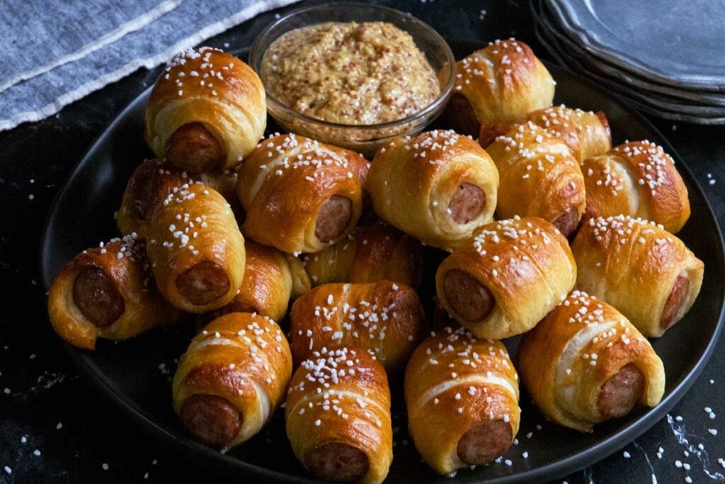 Sausage pretzel bites with mustard on a black plate.