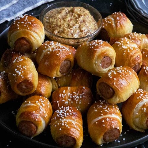 Sausage pretzel bites with mustard on a black plate.