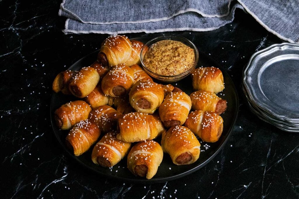 sausage pretzel bites on a black plate with serving dishes