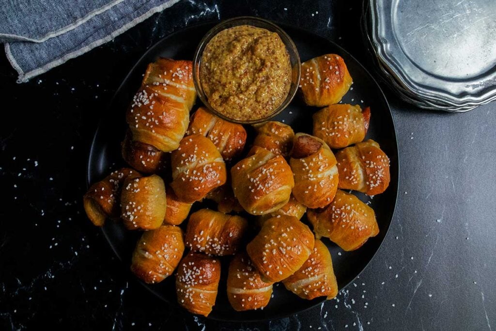 Sausage pretzel bites on a black plate with stone ground mustard garnish