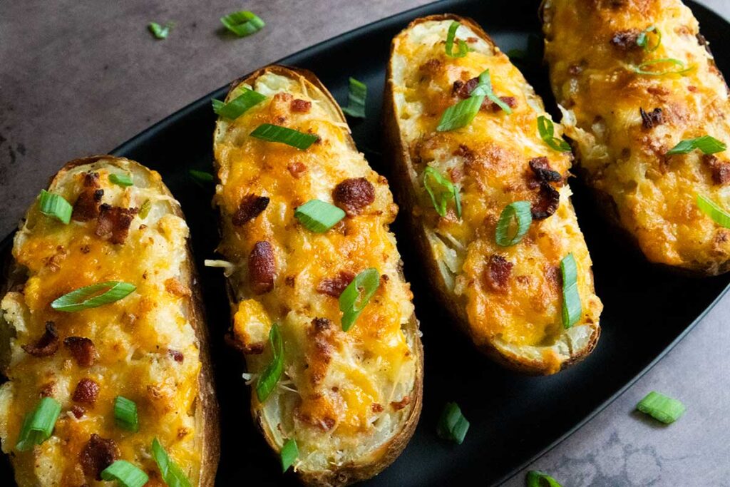 Twice baked potatoes on an oval black platter garnished with diced green onions.