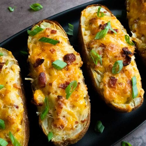 Twice baked potatoes on an oval black platter garnished with diced green onions.