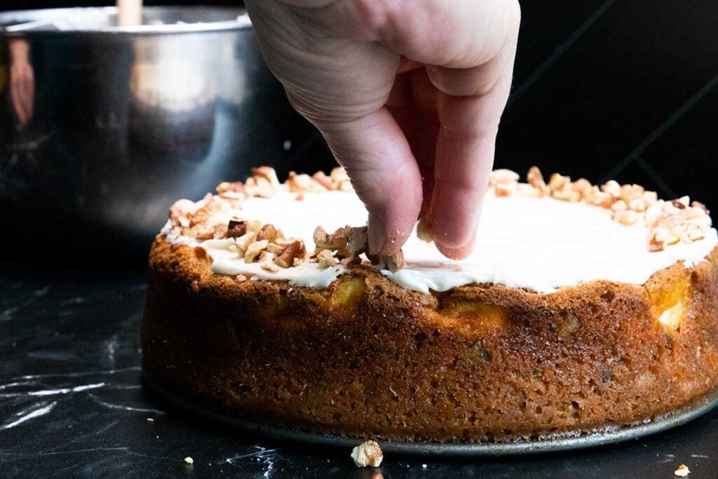 garnishing the carrot cake cheesecake with chopped pecans