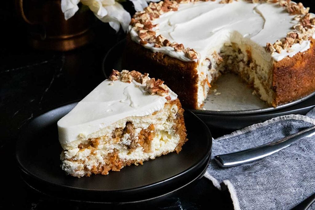 Slice of carrot cake cheesecake on black plate.