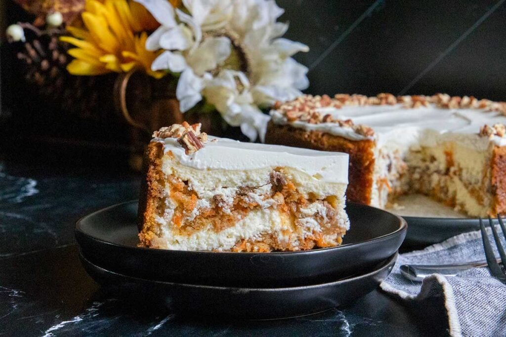 A slice of carrot cake cheesecake on black plate.