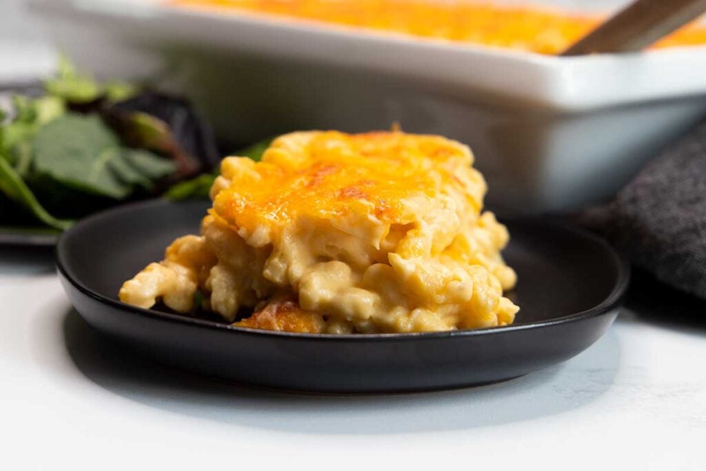 A serving of baked macaroni and cheese on a black plate.