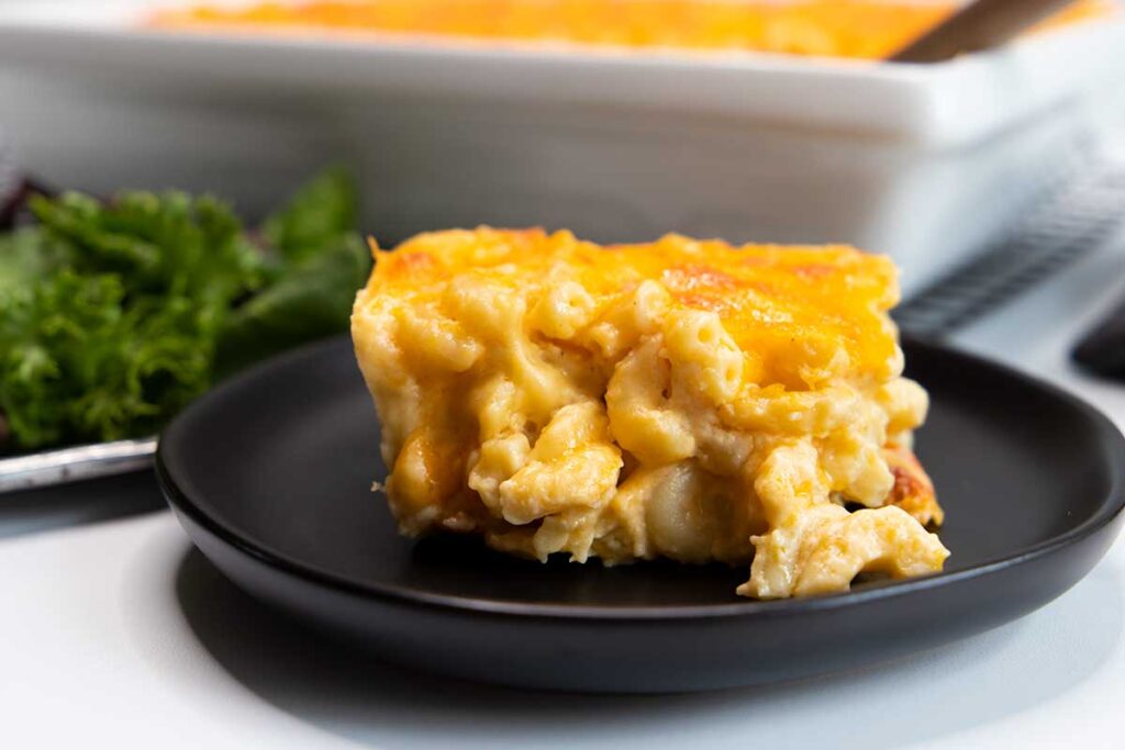 A serving of baked macaroni and cheese on a black plate.