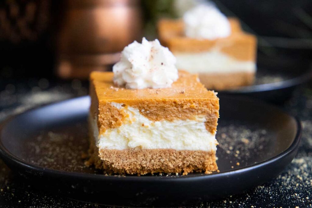 Pumpkin cheesecake bars on a black plate.