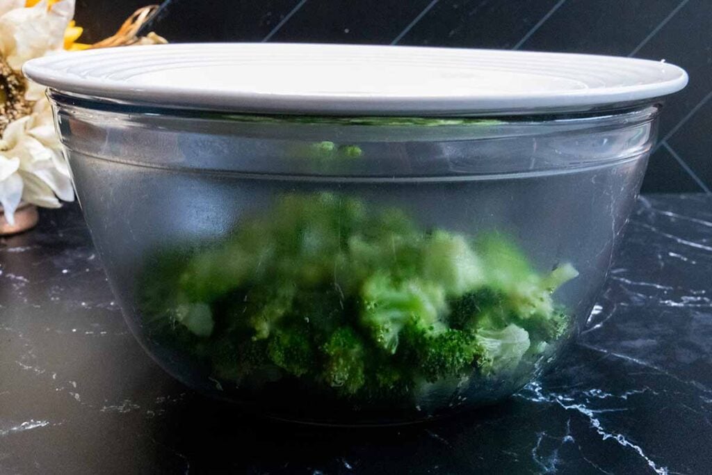 Fresh broccoli in a glass bowl with a plate on top as a lid.