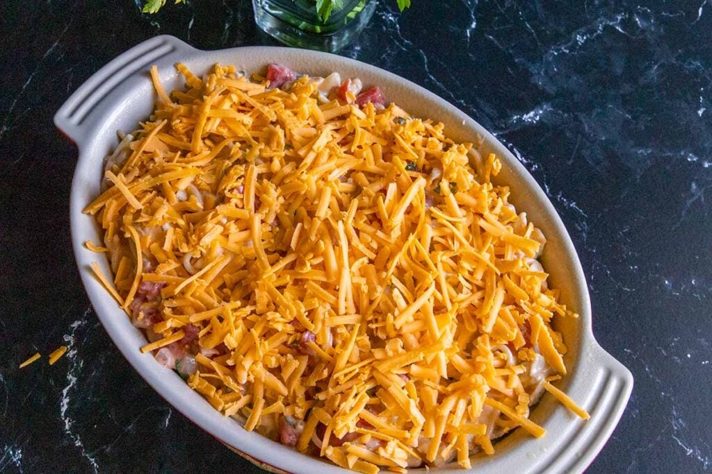 unbaked chicken spaghetti in a casserole topped with shredded cheese