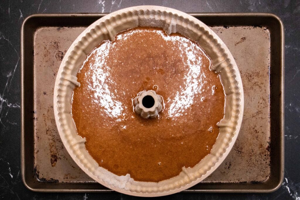 Gingerbread batter in bundt pan on a baking sheet.