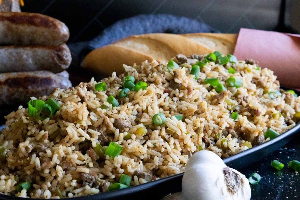 Cajun dirty rice in an oblong dish with a loaf of bread in the background.