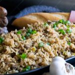 Cajun dirty rice in an oblong dish with a loaf of bread in the background.