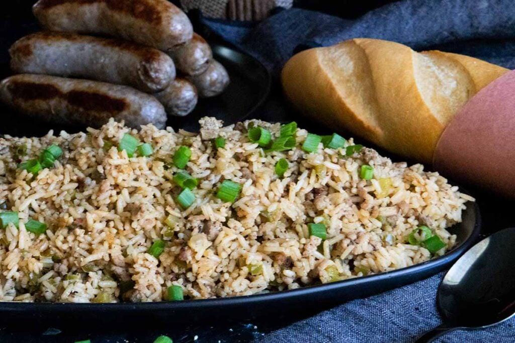 Cajun dirty rice in a black bowl with sausages and bread