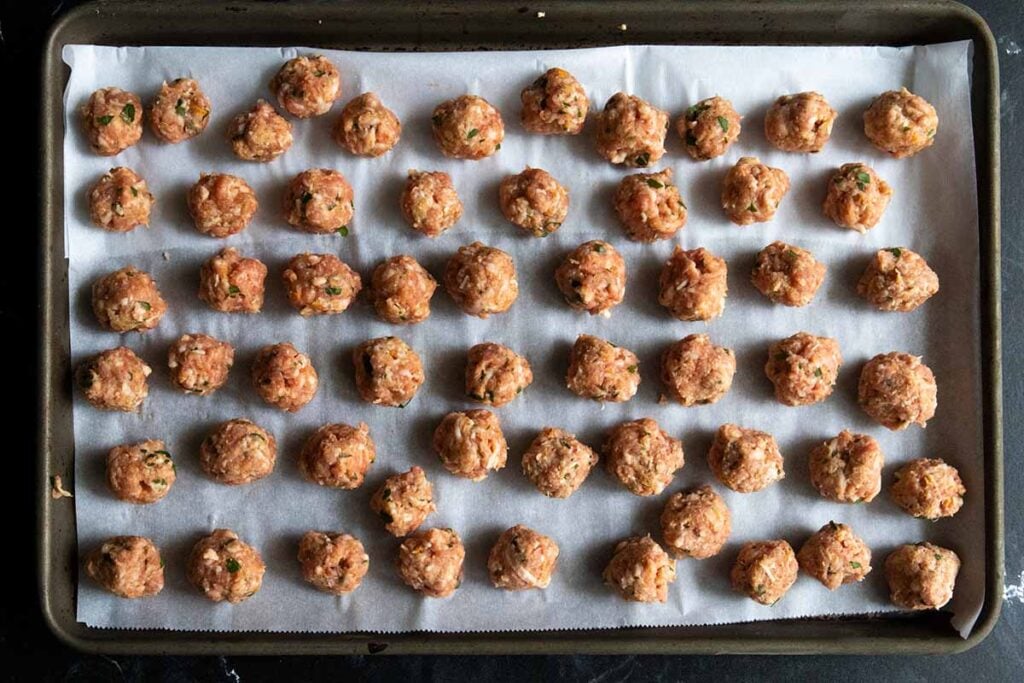 Tiny meatballs on a parchment lined baking sheet.