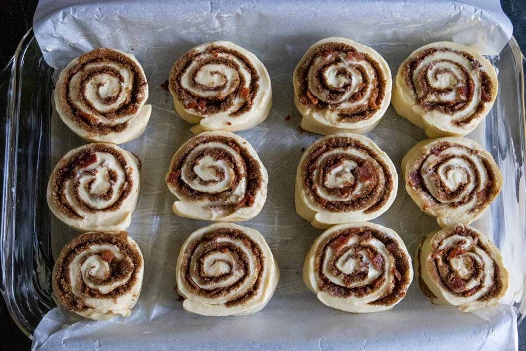 Maple bacon cinnamon rolls unproofed in a parchment paper lined baking dish.