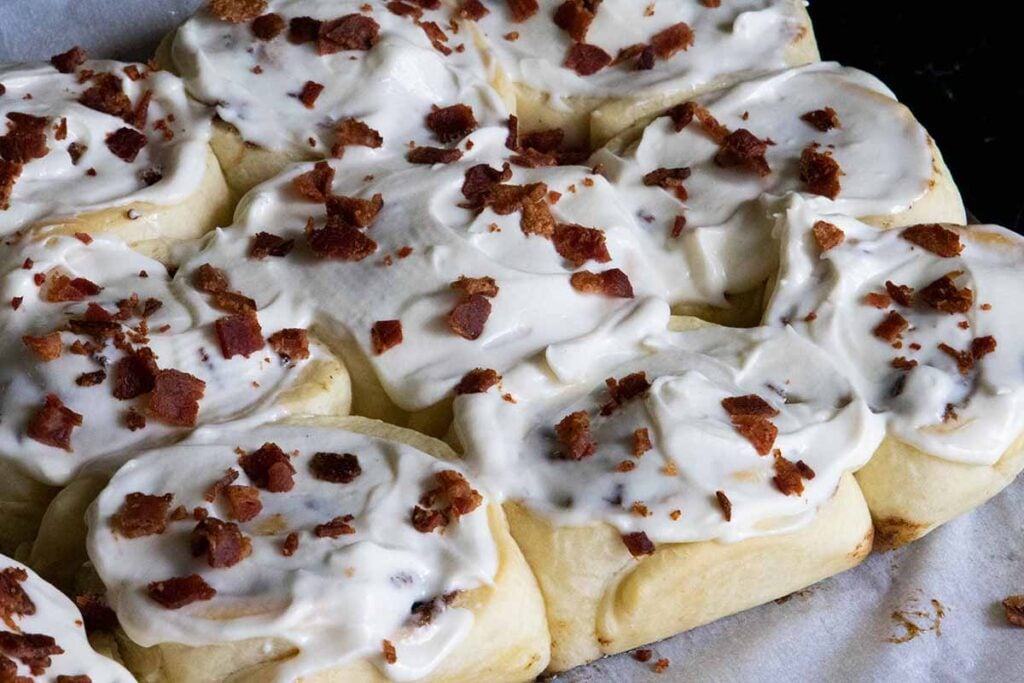 Maple bacon cinnamon rolls on a parchment paper lined wooden board.