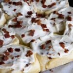 Maple bacon cinnamon rolls on a parchment paper lined wooden board.