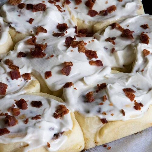 Maple bacon cinnamon rolls on a parchment paper lined wooden board.