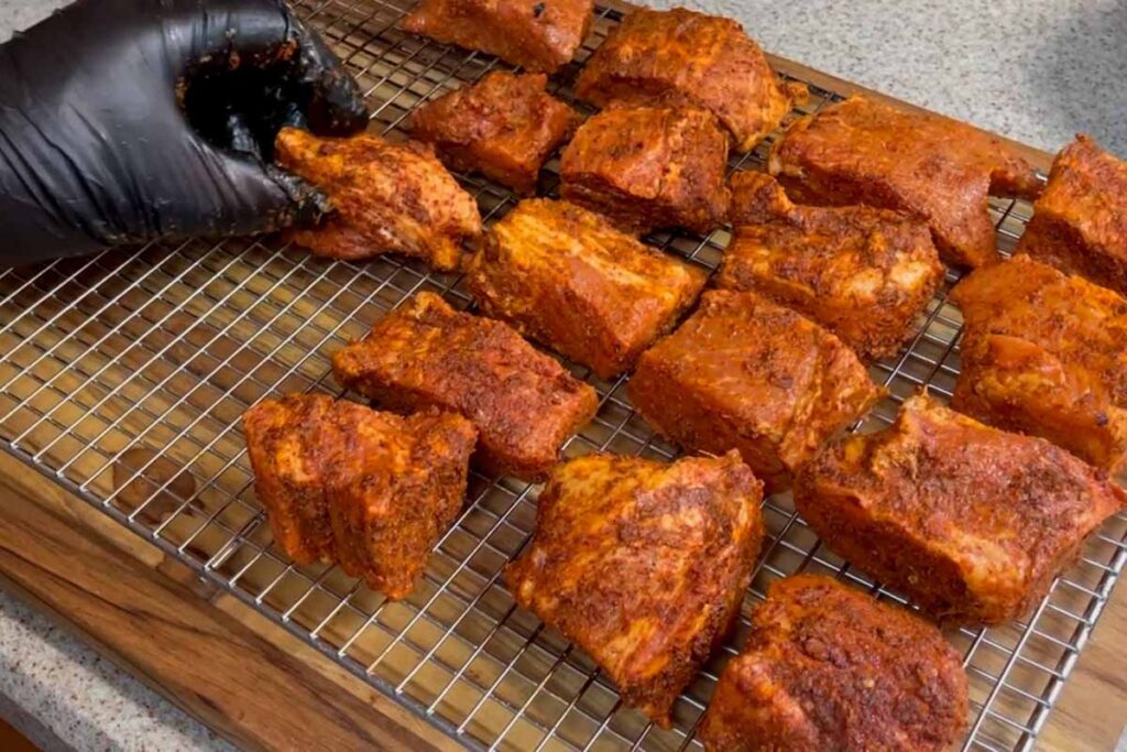 placing cubes of pork butt with rub onto bradley rack