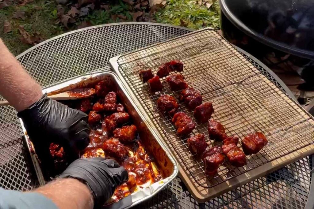 Placing sauced up pork butt burnt ends back onto a bradley rack