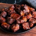 Pork butt burnt ends piled on a black plate on top of wooden board.