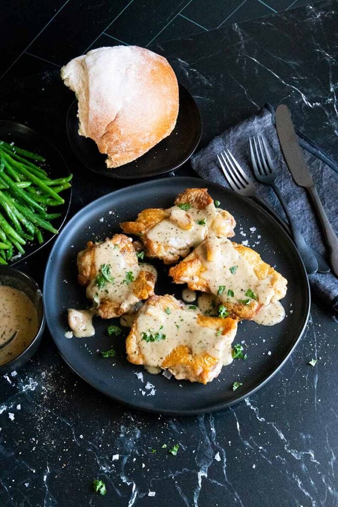 Crispy boneless chicken thighs with a creamy garlic sauce. Bread and green beans in the background