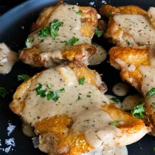 Crispy boneless chicken thigh with a garlic cream sauce on a black plate.