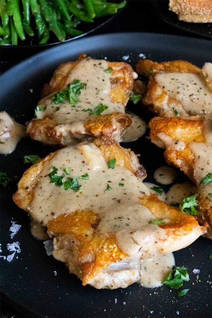 Crispy boneless chicken thigh with a garlic cream sauce on a black plate.