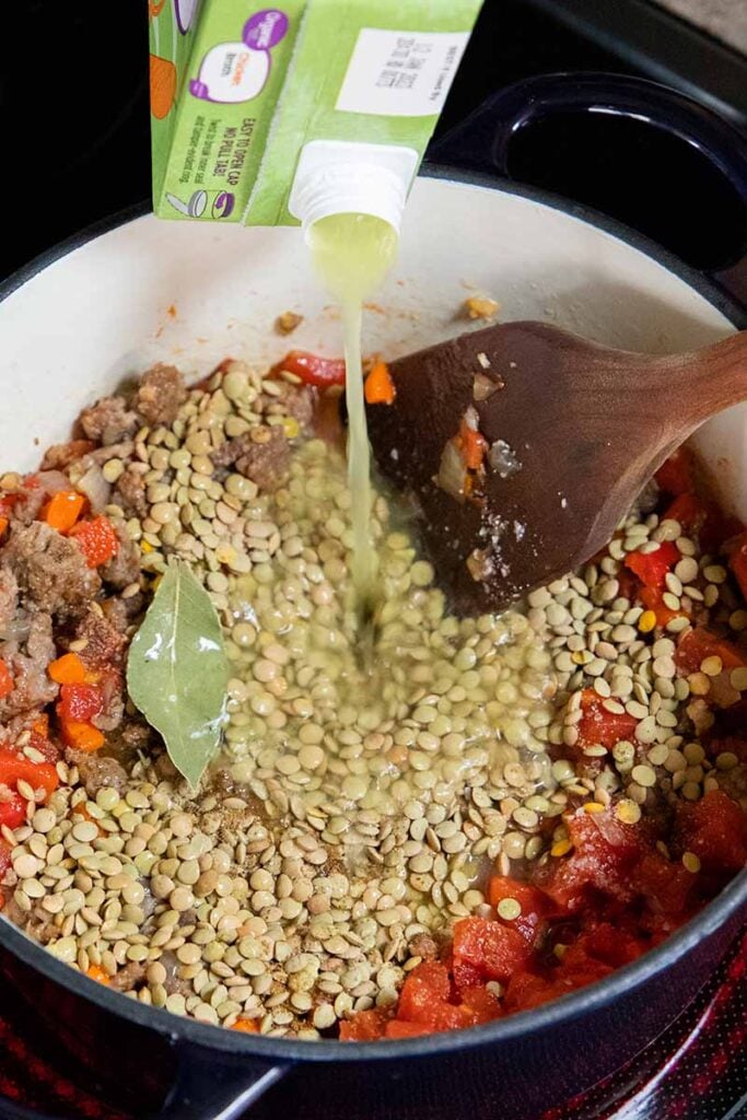 Soup ingredients in a dutch oven with stock being poured in.