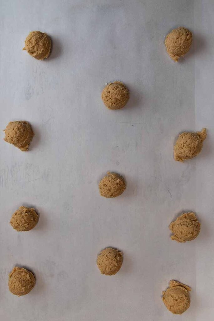 Cookie dough balls on a parchment lined baking sheet.