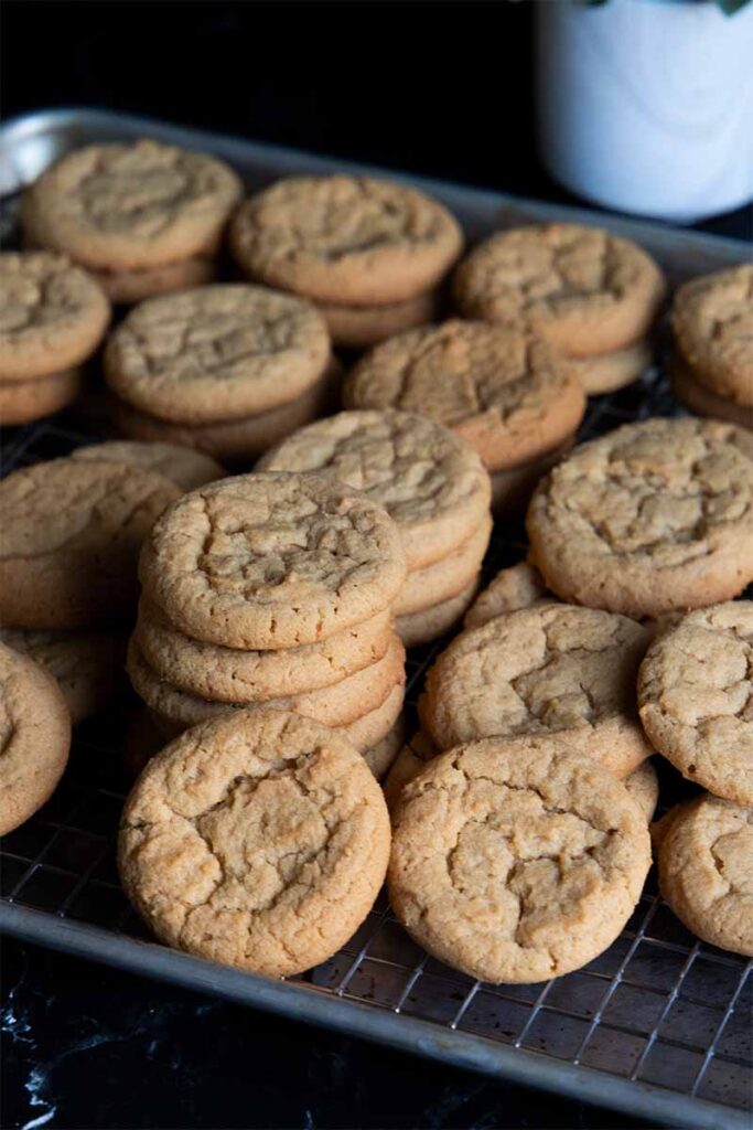 Peanut butter cookies stacked on a wire rack in a baking sheet.