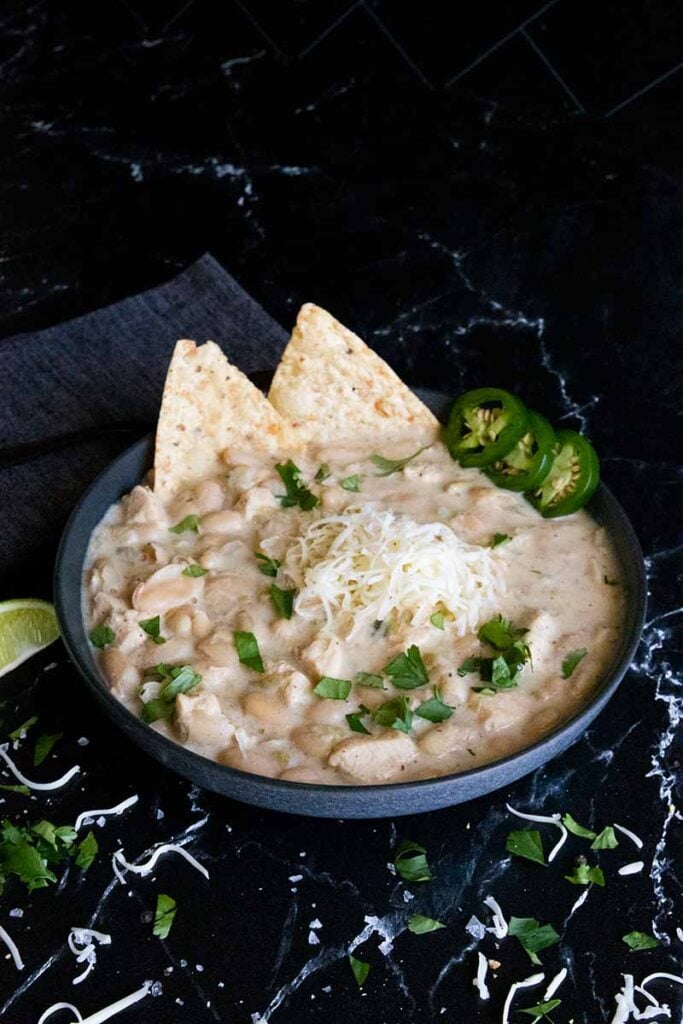 White chicken chili in a black bowl garnished with jalapenos and cilantro