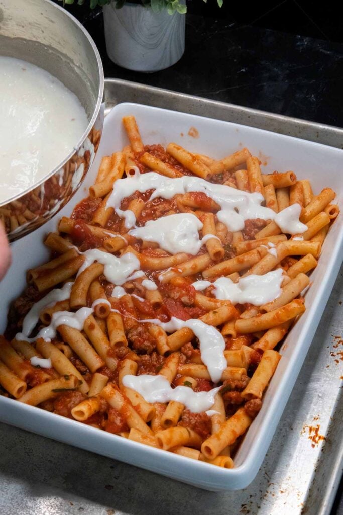 adding bechamel to the ziti casserole dish