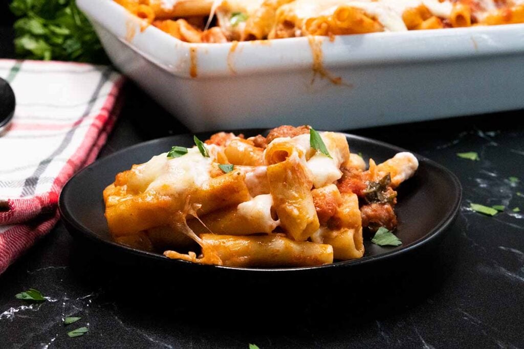 Baked ziti with a serving on a dark plate.