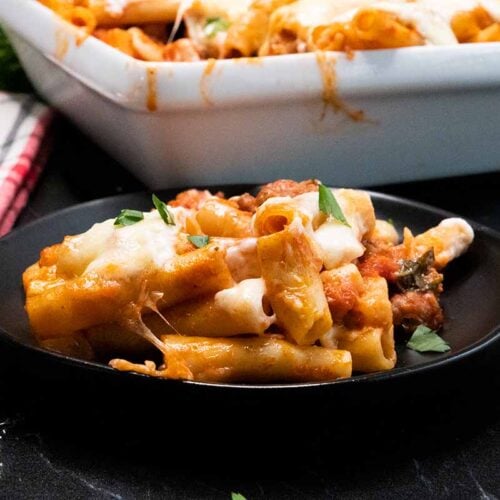 Baked ziti with a serving on a dark plate.