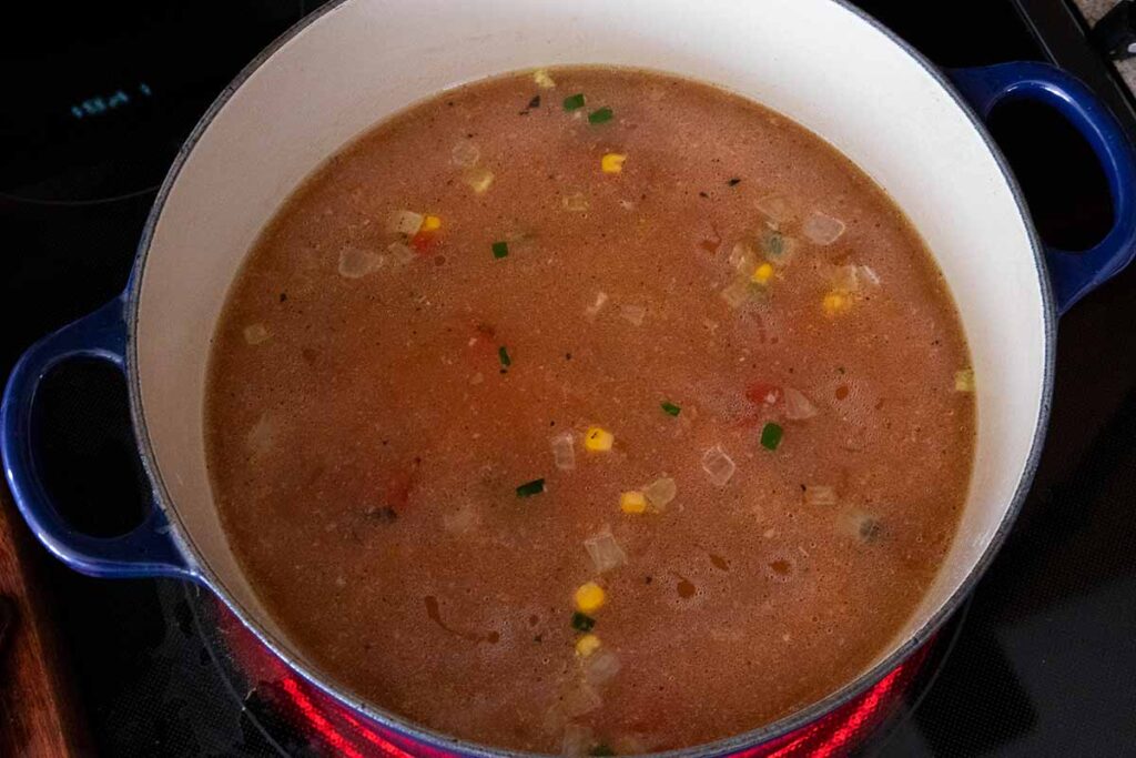 Ingredients for chicken tortilla soup cooking in a blue dutch oven