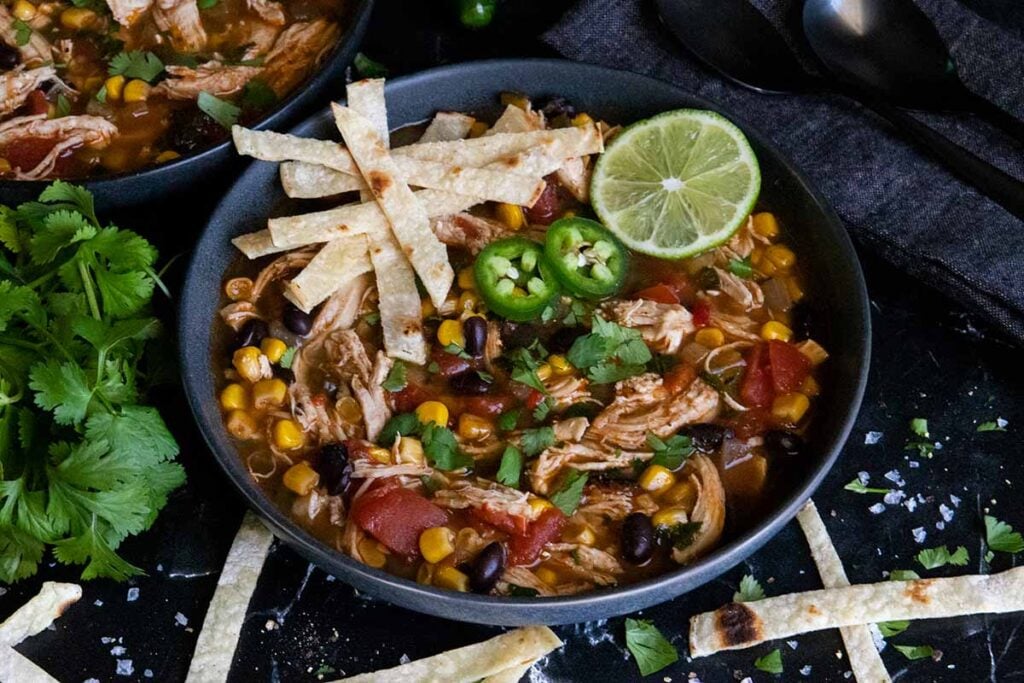 Chicken tortilla soup prepared on the stovetop with cilantro and various other garnishes.