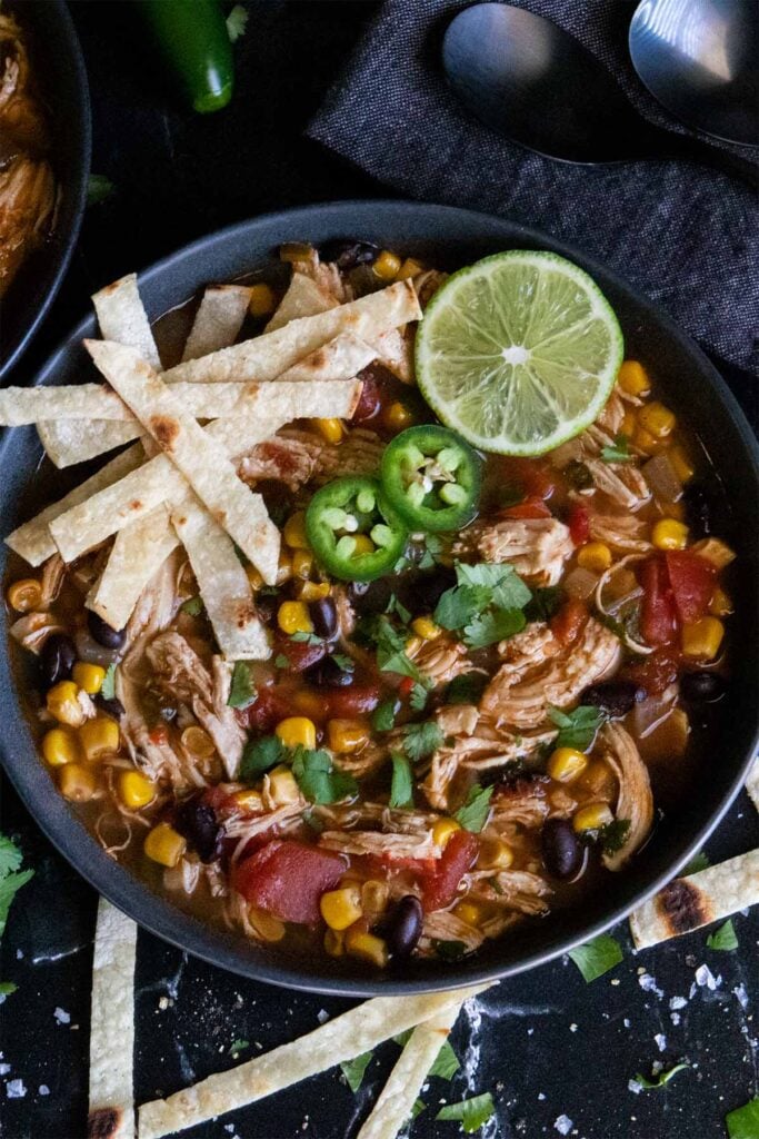 Chicken tortilla soup in a dark bowl with all sorts of garnish