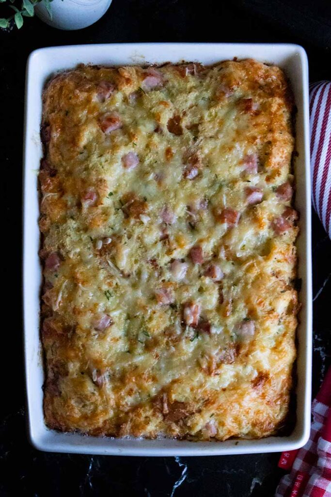 Baked ham and cheese strata in a baking dish on a dark surface.