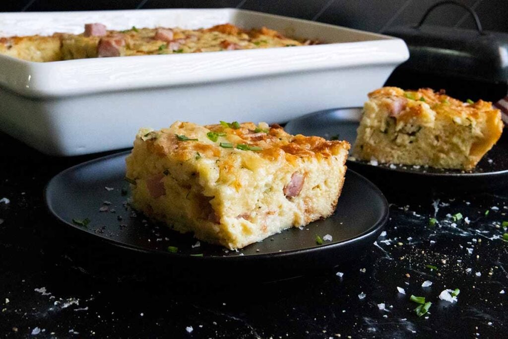 Ham and cheese strata slice on black plate.