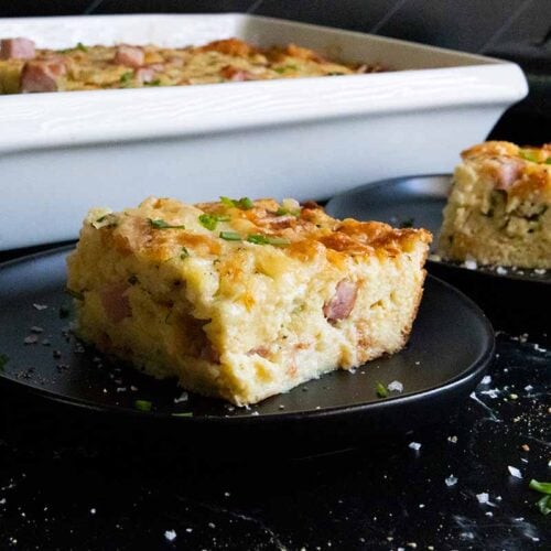 Ham and cheese strata slice on black plate.