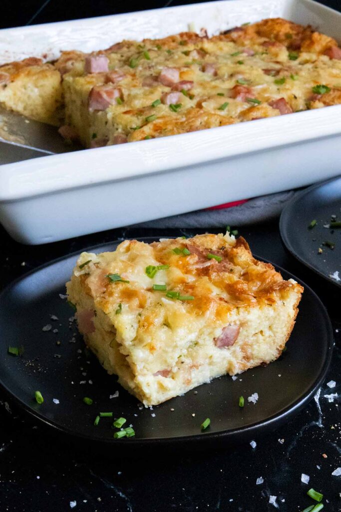 Ham and cheese strata slice on black plate garnished with chives.