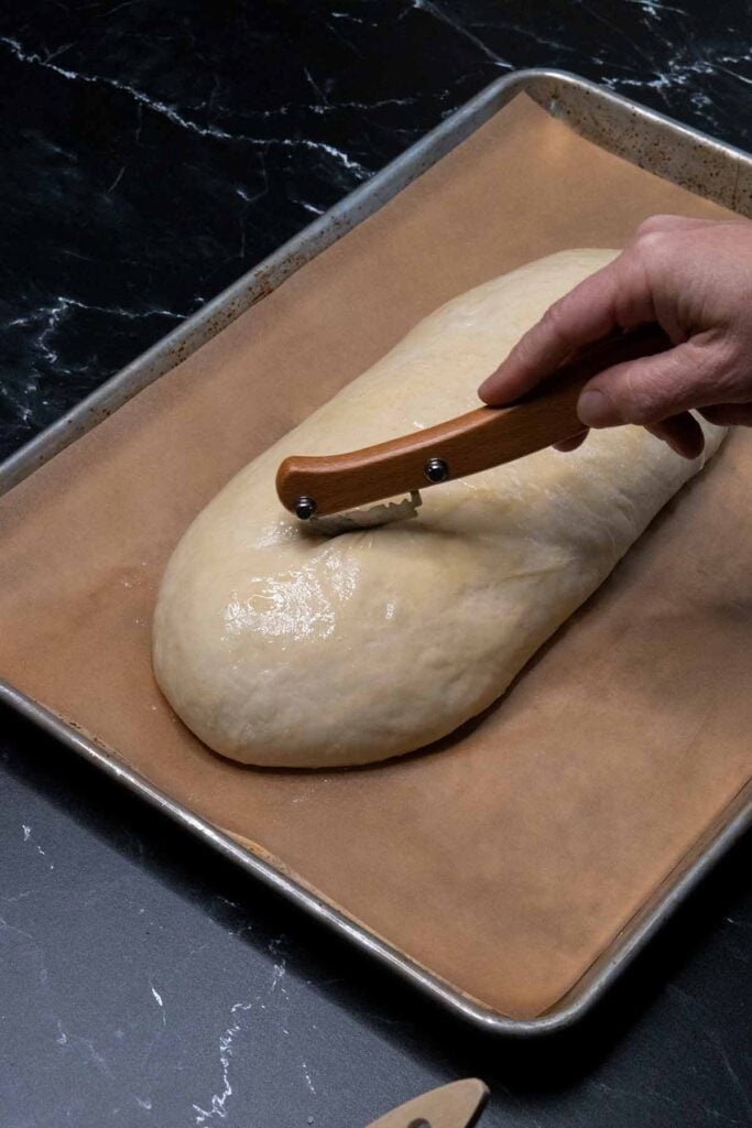 cutting slices into an unbaked loaf of italian bread.