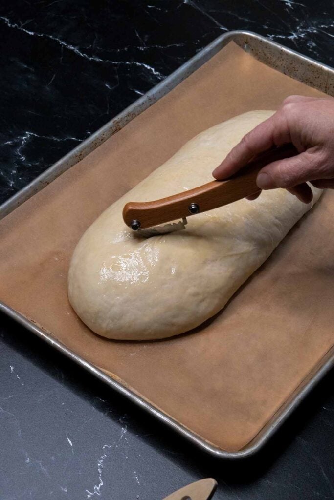 Cutting slices into an unbaked loaf of Italian bread.