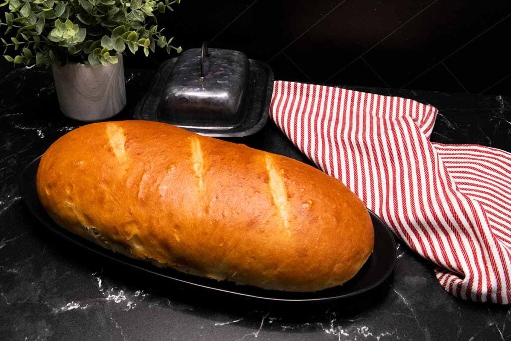 A baked loaf of Italian bread on a black plate with a red and white towel lying next to it.
